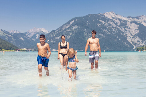 A family with children bathing in the turquoise blue Lake Achensee in Maurach and enjoying the sunny weather.